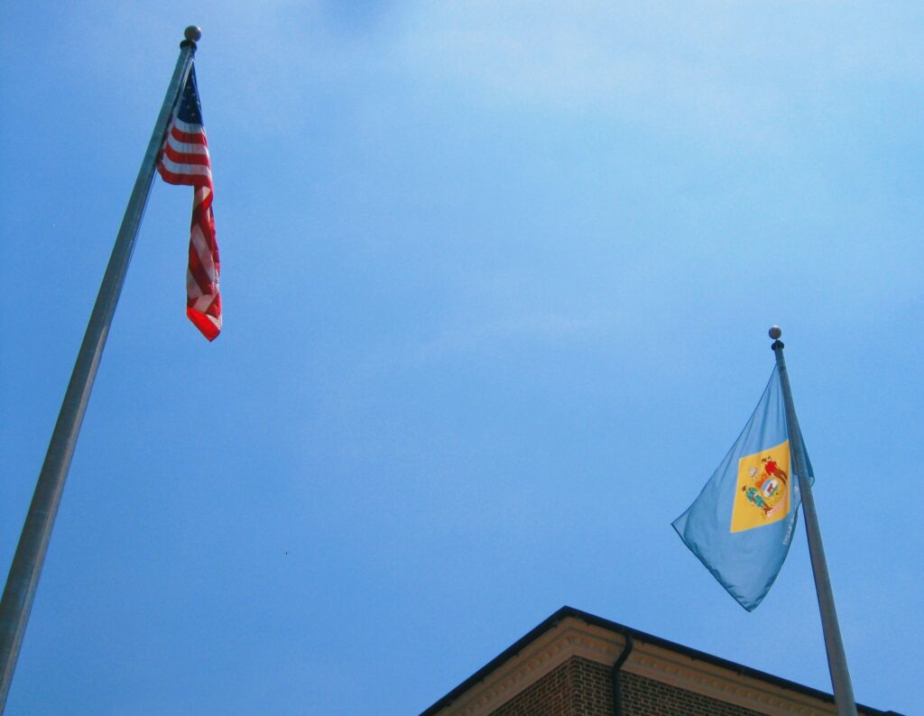 The United States and Delaware flags waving against a beautiful blue sky in Dover, DE, symbolizing the state-pride and national excellence in dental marketing services offered by Clear to Launch Dental Marketing for Dover's dental practices.