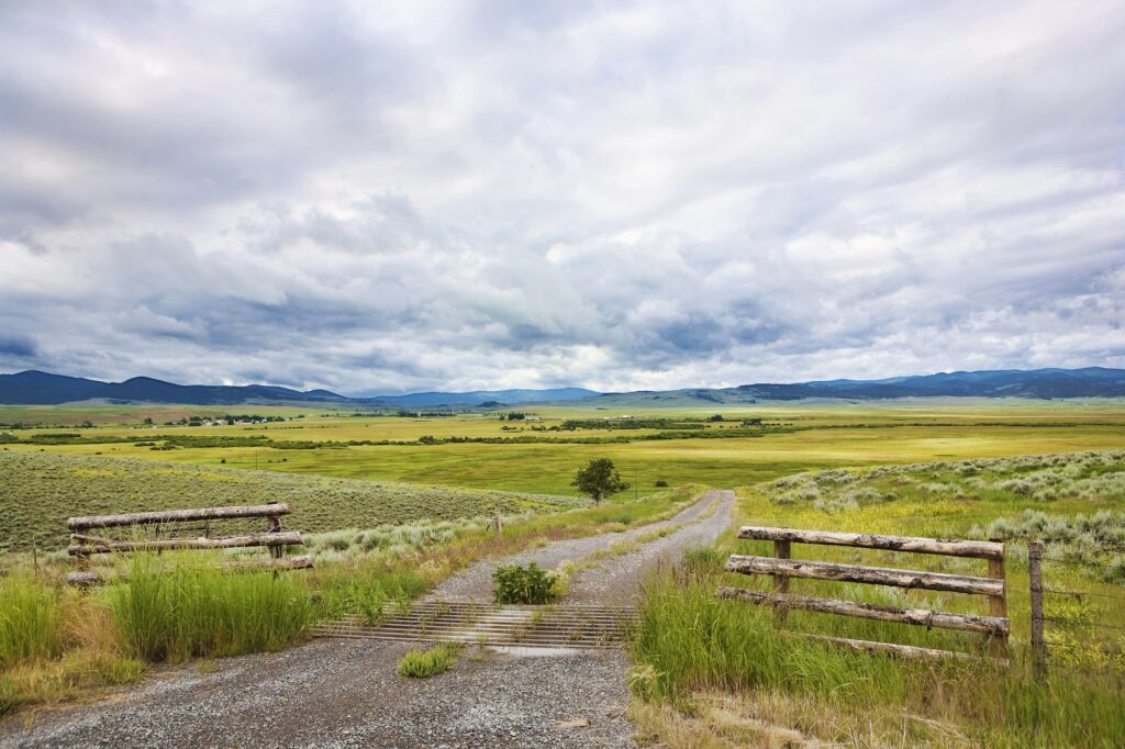 Open grassland, fences, dirt road, and clouds in the Montana landscape near Missoula, MT, illustrating the vast beauty of Big Sky Country and Clear to Launch Dental Marketing' strategic dental marketing initiatives tailored for Missoula dental practices.