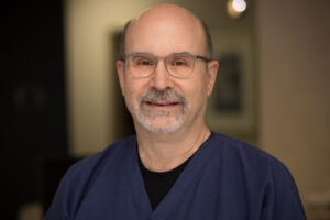 Headshot of Dr. Dalin from Dalin Dental Associates, wearing navy scrubs in a warmly lit dental office