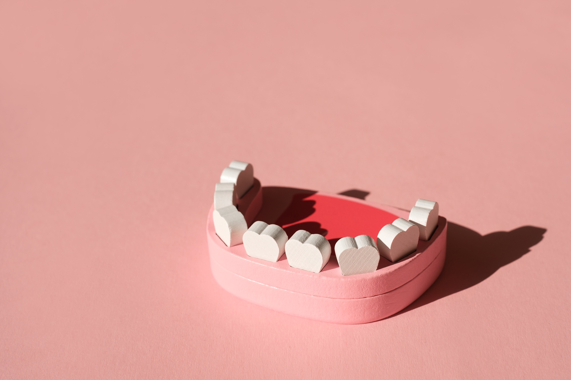 Creative dental concept featuring a dental model with heart-shaped teeth on a pink background, symbolizing patient care and the importance of dental marketing and advertising.