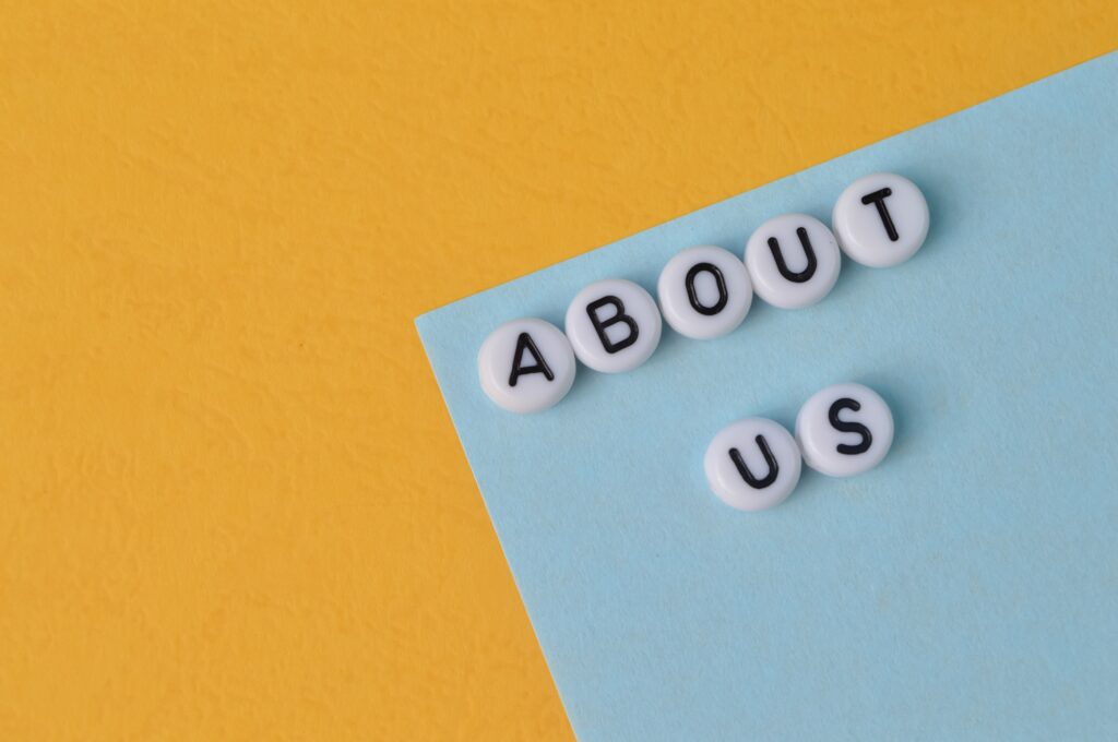 Flat lay of white letter beads spelling 'About Us' on blue and yellow background – representing healthcare practice storytelling and team introduction