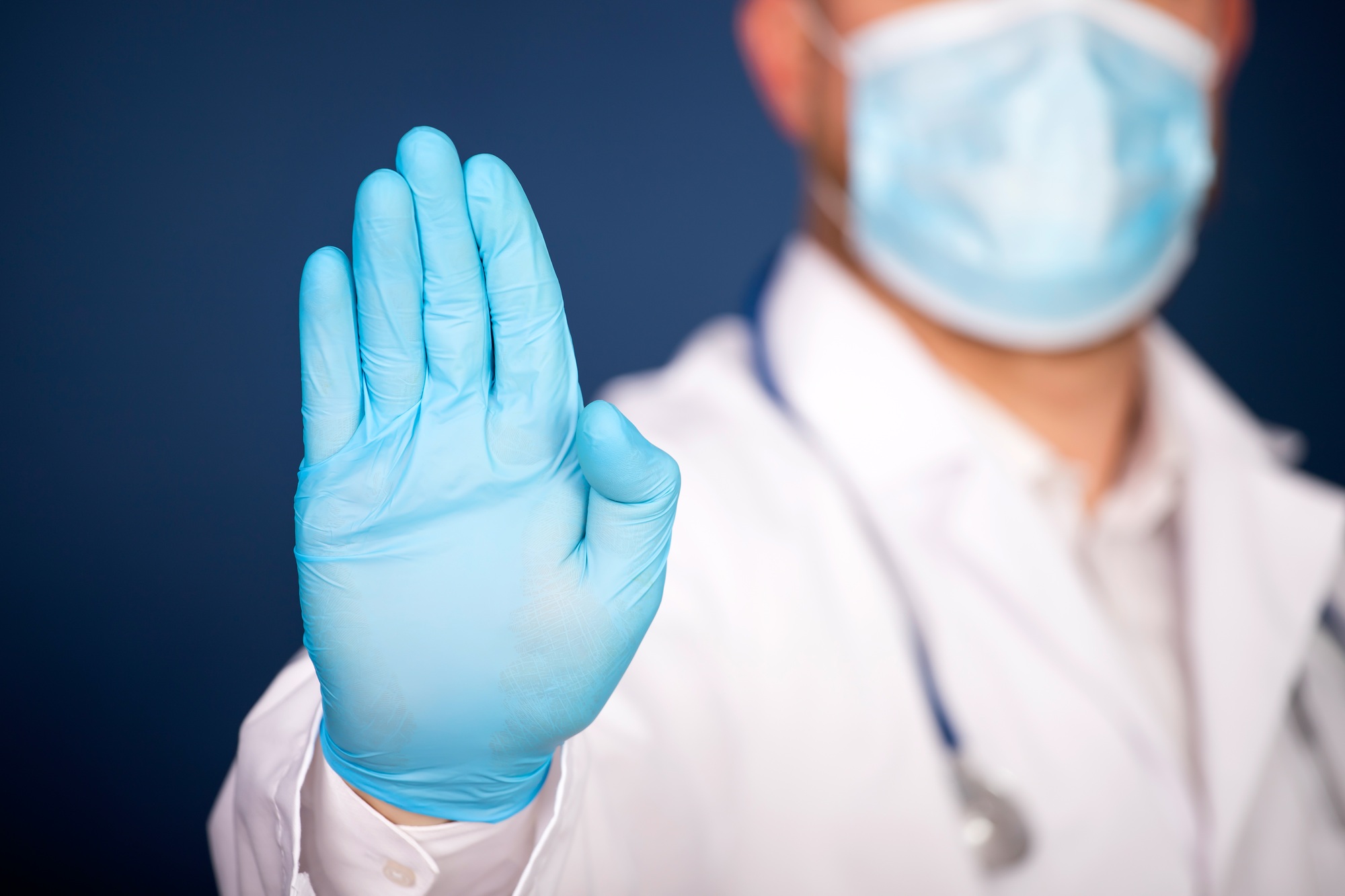 Dentist wearing a mask and gloves holding up hand to signal stop, symbolizing how negative keywords prevent unqualified traffic in dental Google Ads campaigns