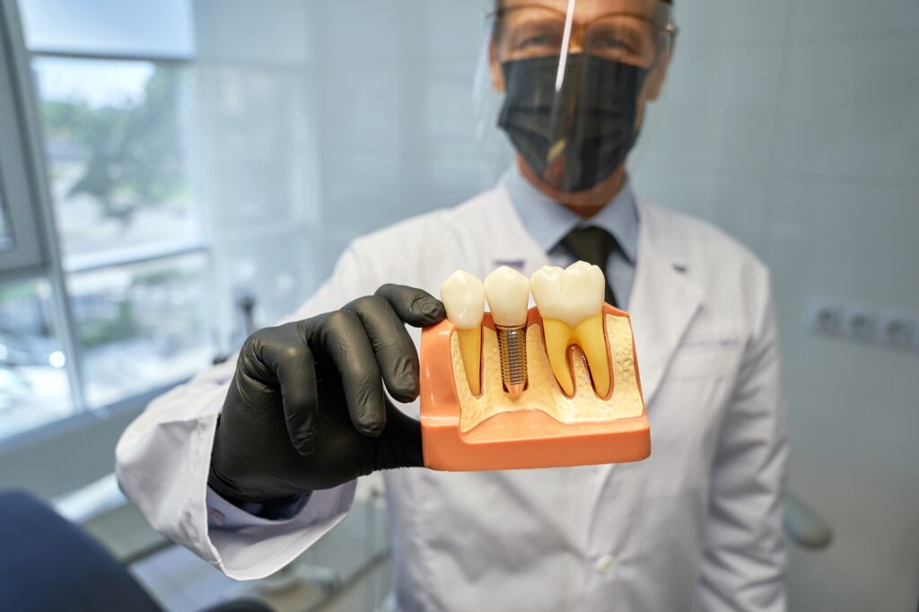 Dentist holding dental implant model during patient education, featured in blog on dental implant marketing strategies