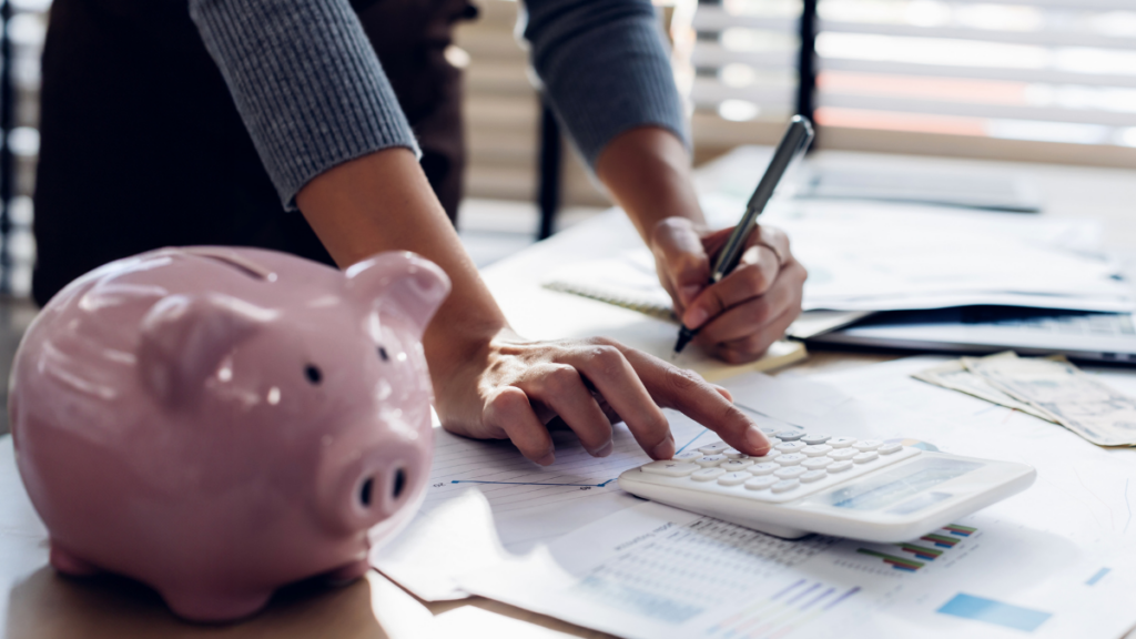 person calculating a healthcare marketing budget for a startup or acquisition with a piggy bank and financial documents for Clear to Launch Healthcare Marketing